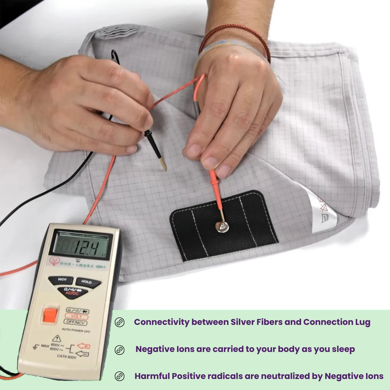 Person testing connectivity between silver fibers and the earthing lug with a digital meter displaying voltage throughput