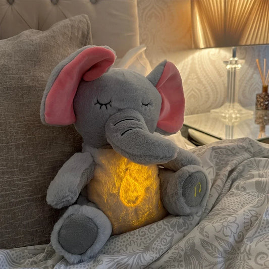 Plush breathing elephant night light on a bed with warm glow