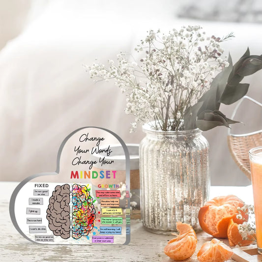Motivational acrylic plaque with brain diagram and affirmations on a table with oranges and flowers.