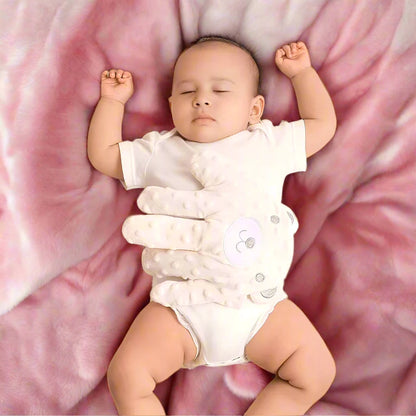 Baby in a white onesie lying on a pink blanket with the HushHand in place