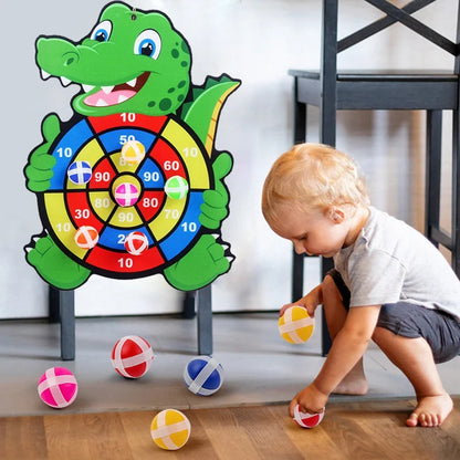 Toddler picking up sticky balls with a colorful target board shaped like a crocodile mounted on a chair.