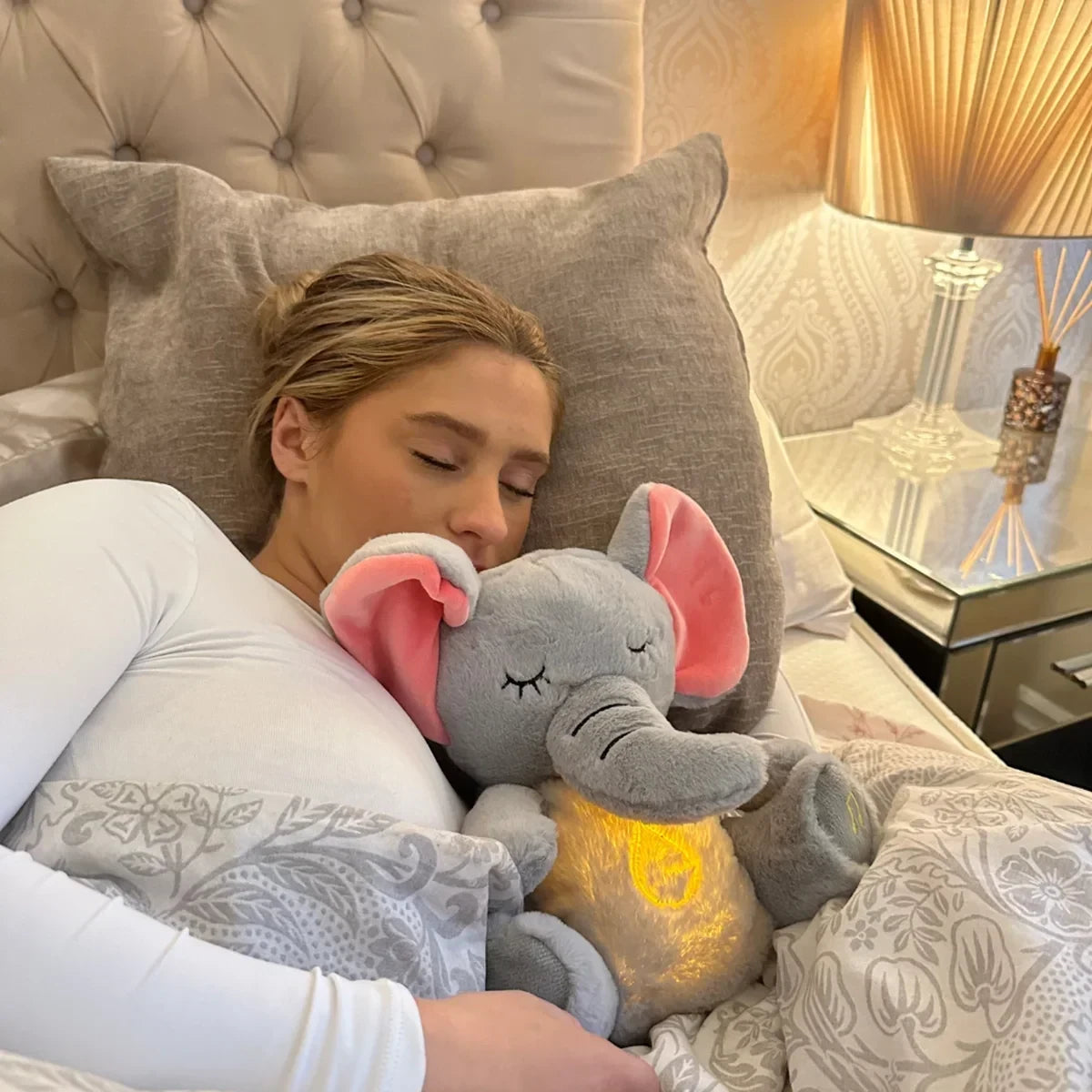 Woman lying in bed with a glowing elephant plush toy