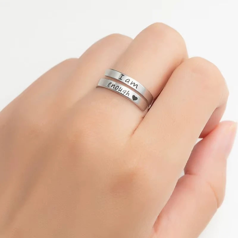 Silver ring with 'I am enough' laser etched on a hand against a white background