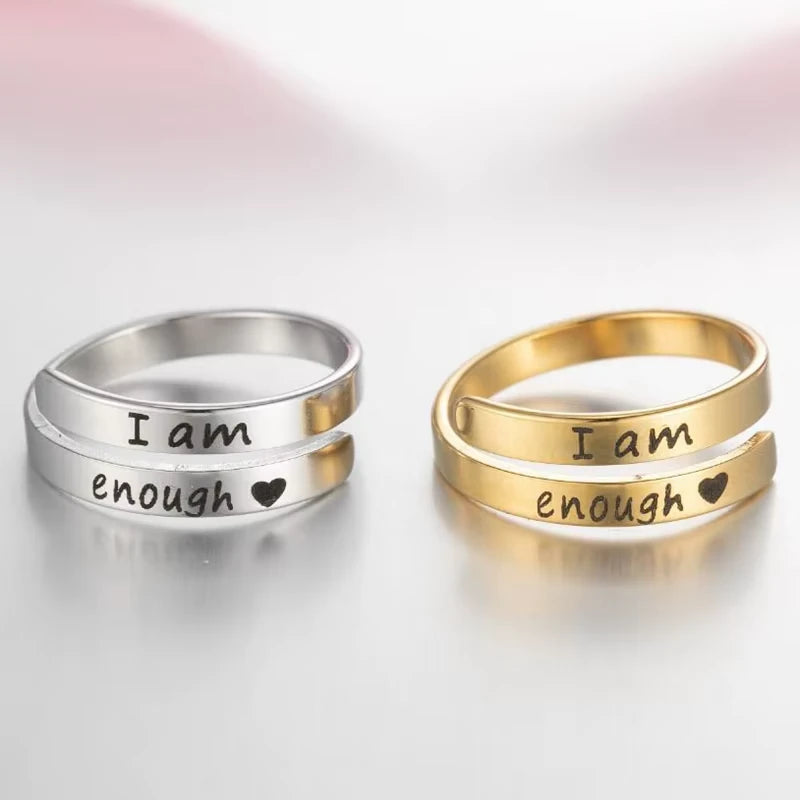 Two rings, one silver and one gold, with 'I am enough' laser etched on, on a light background.