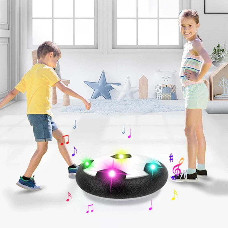 Two children playing with a hover soccer ball in a room with a window and decorative items.