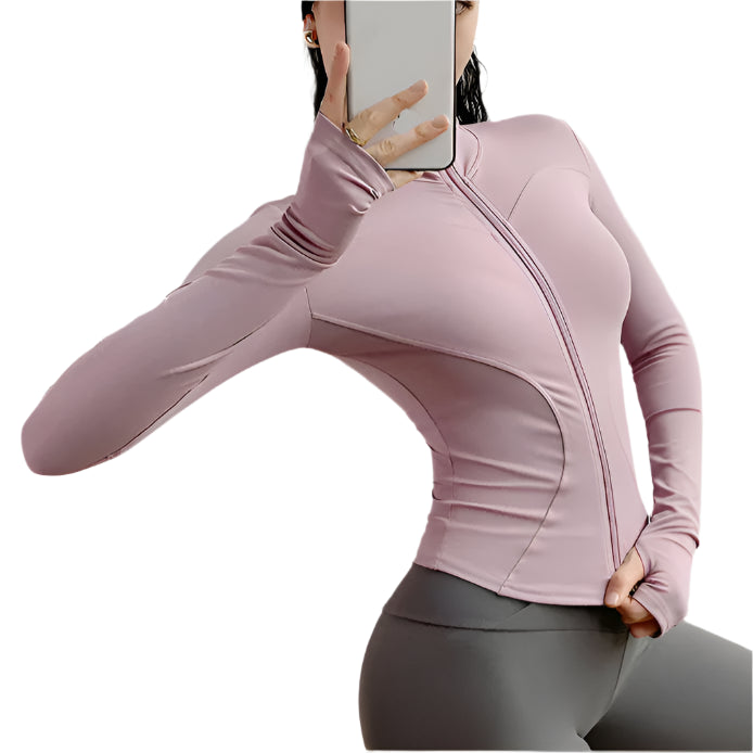Woman wearing a pink zip up thumb hole jacket and gray leggings taking a  selfie against a white background 