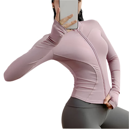 Woman wearing a pink zip up thumb hole jacket and gray leggings taking a  selfie against a white background 