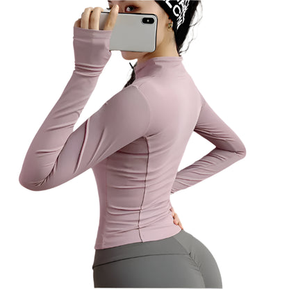 Woman wearing a pink zip up thumb hole jacket and gray leggings taking a  selfie from the side against a white background 