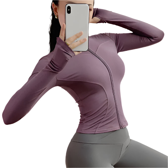 Woman wearing a purple zip up thumb hole jacket and gray leggings taking a selfie against a white background 