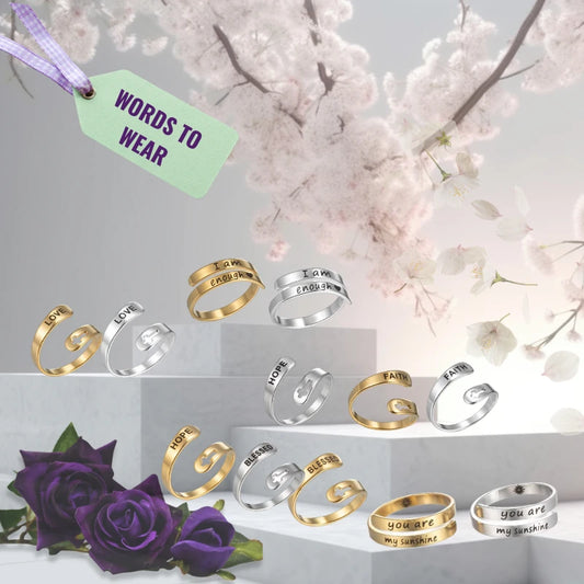 Collection of gold and silver rings with validation messages laser etched on, shown on a light gray background with cherry blossoms and purple roses.