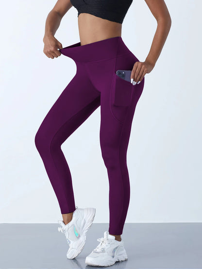 Woman wearing dark purple high waist leggings with a side pocket and phone inside the pocket showing stretchable fabric with a light background