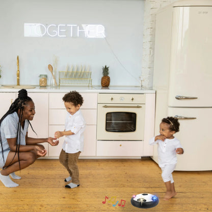 Woman and two children playing with the hover soccer ball in a kitchen.